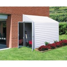 a small white shed sitting on top of a lush green field next to a brick building