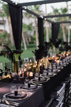 a long table is set up with black and white place settings, candles and flowers