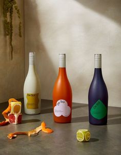 three different colored bottles sitting on top of a counter next to oranges and other fruit