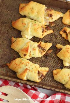 several pieces of pizza on a baking sheet with a wooden spoon and red checkered table cloth