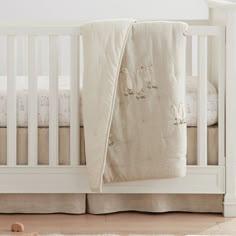 a white crib with two pillows and a blanket on the floor in front of it