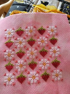 a cross stitch project with strawberries and daisies on pink fabric, sitting on a table