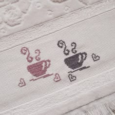 two cross stitch coffee mugs on a white tablecloth