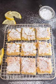 lemon bars cooling on a wire rack with powdered sugar and lemons around them