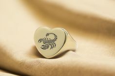 This 14k gold heart-shaped ring features an engraved scorpion, symbolizing power and intensity, ideal for those born under the Scorpio zodiac sign. The custom design offers a bold statement, making it a unique accessory for women who love astrological jewelry. Crafted with care, this personalized ring adds elegance and meaning to your collection, perfect for zodiac enthusiasts or as a distinctive gift. 📏 Ring Size: Choose your preferred size from the drop-down menu. 💍 Signet Details: Signet Size: 16mm Signet Shape: Heart Metal Type (Main Photo): 14k Gold Filled - Other options available in the drop-down menu. Texture / Finish (Main Photo) - Shiny - Other options available in the drop-down menu. 🌟 Why Choose Our Unique Handmade Jewelry? ♥ Nickel-Free ♥ Tarnish Resistant ♥ One-Year Warran Astrological Jewelry, Scorpio Ring, Scorpion Ring, Dna Jewelry, Scorpio Zodiac Sign, Heart Shaped Ring, Zodiac Scorpio, Animal Ring, Ring Heart