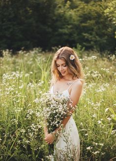 a woman in a white dress is standing in tall grass with flowers on her head