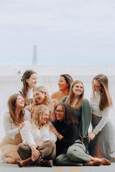 a group of women sitting next to each other on top of a cement slab in front of the ocean