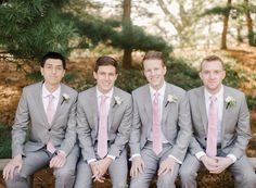 a group of men sitting next to each other on top of a wooden bench in front of trees