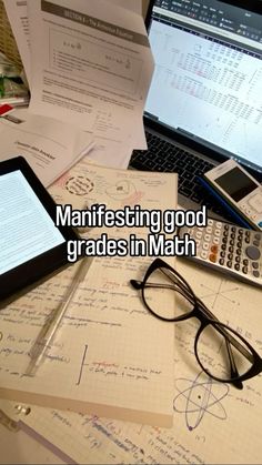 a desk with papers, calculator and laptops on it that read manifesting good grade in math