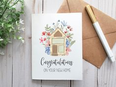 a card that says congratulations on your new home next to a pen and envelope with flowers