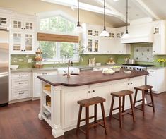 a large kitchen with white cabinets and wooden counter tops, along with two stools in front of the island