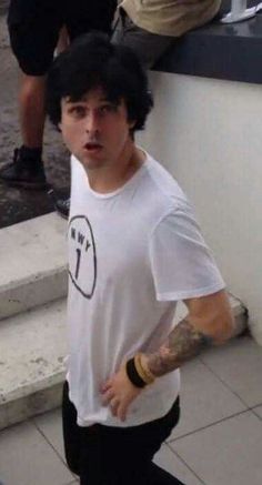 a man with tattoos on his arm standing in front of some stairs and looking at the camera