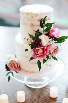 a white wedding cake with pink flowers and candles on a table in front of it