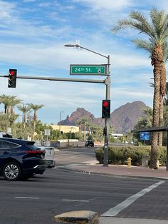 a car is stopped at an intersection with palm trees and mountains in the back ground