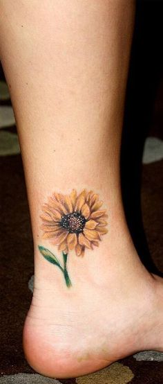 a sunflower tattoo on the foot of a woman's leg, which is painted with watercolors