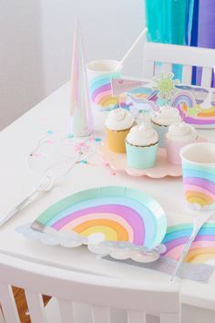 a table set up with cupcakes, rainbow plates and napkins on it