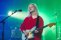 a woman standing in front of a microphone while holding a guitar