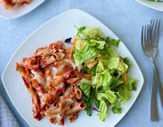 a white plate topped with pasta covered in sauce next to a green salad and fork