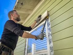 a man is painting the side of a house with paint rollers and a window