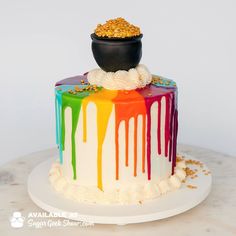 a multicolored cake with gold sprinkles and a black pot on top