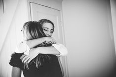 two women hug each other in front of a door and stairs, black and white photograph