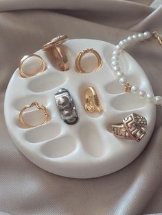 an assortment of rings and bracelets on a white platter with pearl bead necklace