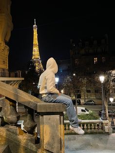 a person sitting on a bench in front of the eiffel tower at night