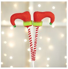 two red and green elf hats on top of a white pole with lights in the background