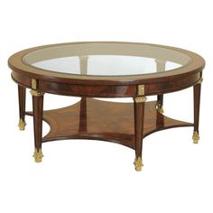 an oval coffee table with glass top and gold trimmings on the bottom shelf