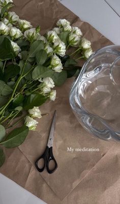 flowers and scissors are sitting on a piece of brown paper next to a glass bowl