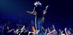 a man standing on top of a stage holding a guitar in front of a crowd