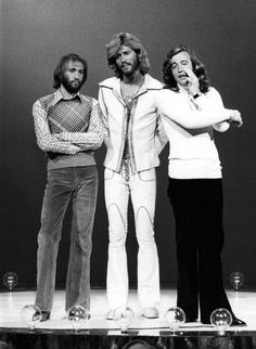 the bee gees are standing on stage with their arms crossed