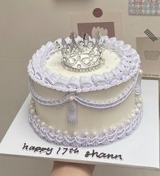 a birthday cake with a tiara on top is being held up by someone's hand