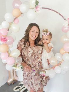 a woman holding a baby in front of a balloon arch with flowers and balloons on it