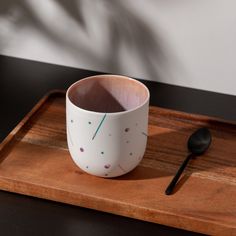 a white coffee cup sitting on top of a wooden tray next to a black spoon