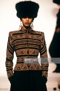 a model walks down the runway in a black and gold outfit with fur on her head