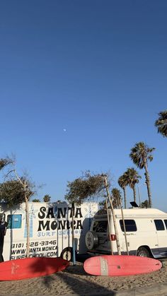 there are surfboards on the beach and in front of a van that is parked next to palm trees