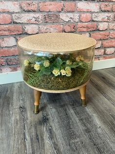 a glass container filled with plants on top of a wooden table next to a brick wall