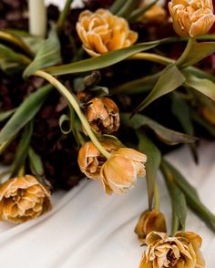 some yellow flowers are sitting on a white table cloth and next to a candle that is lit