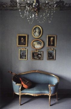 a blue couch sitting under a chandelier next to pictures on the wall