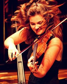 a woman playing the violin on stage with her hair blowing in the wind behind her