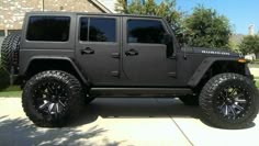 a black jeep is parked in front of a house with large tires and rims