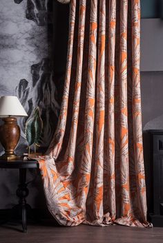 an orange and white curtain hanging in front of a black table with a lamp on it