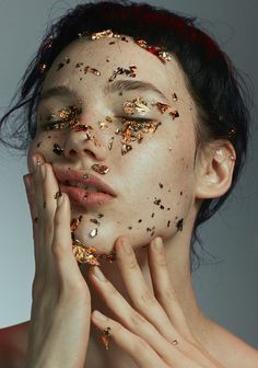 a woman with gold glitter on her face and hands around her face, looking at the camera