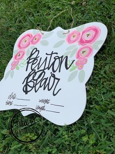 a sign on the grass that says button bear with pink flowers and leaves around it