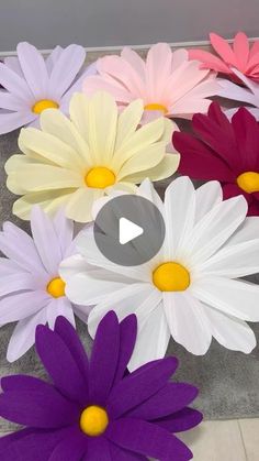 colorful paper flowers on the ground in front of a wall with a video player playing