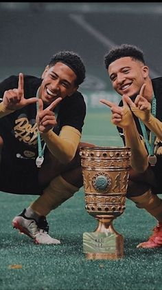 two men posing for the camera with a trophy in front of their backs and hands