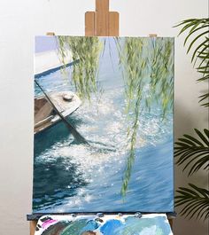 an easel with a painting on it next to a potted plant and water