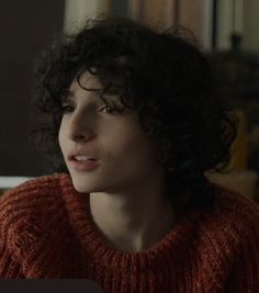 a close up of a person wearing a red sweater and looking off to the side