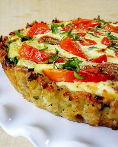 a quiche with tomatoes, cheese and herbs on it sitting on a white plate